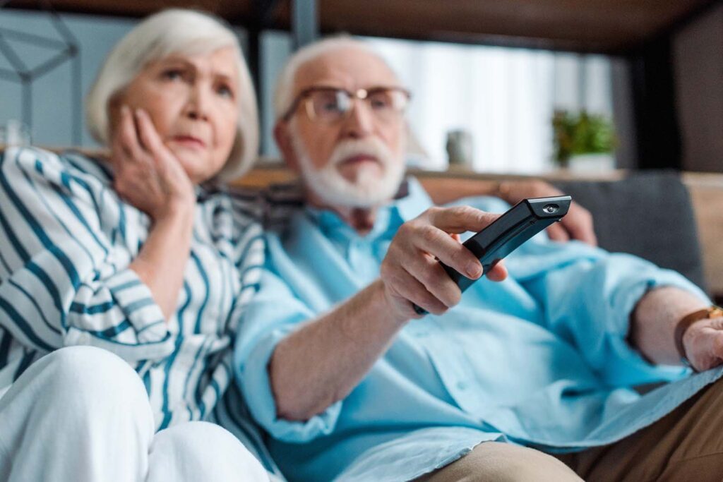 elderly couple watching tv on their couch